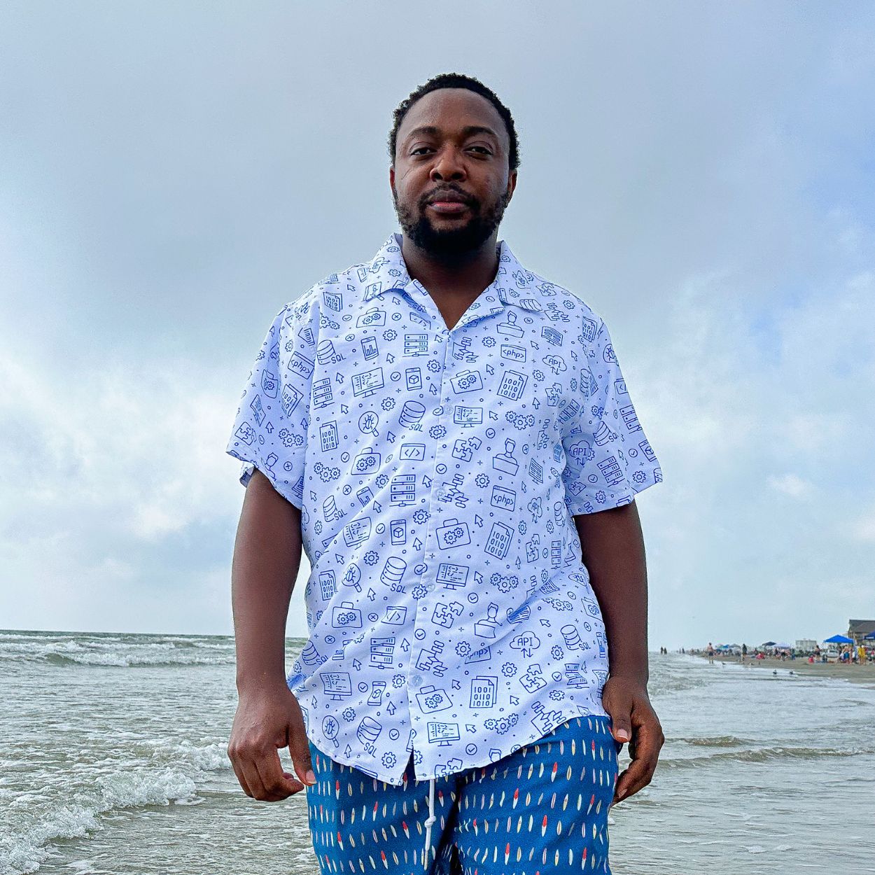 A man is on a beach walking and wearing a geeky software engineer design button up shirt.
