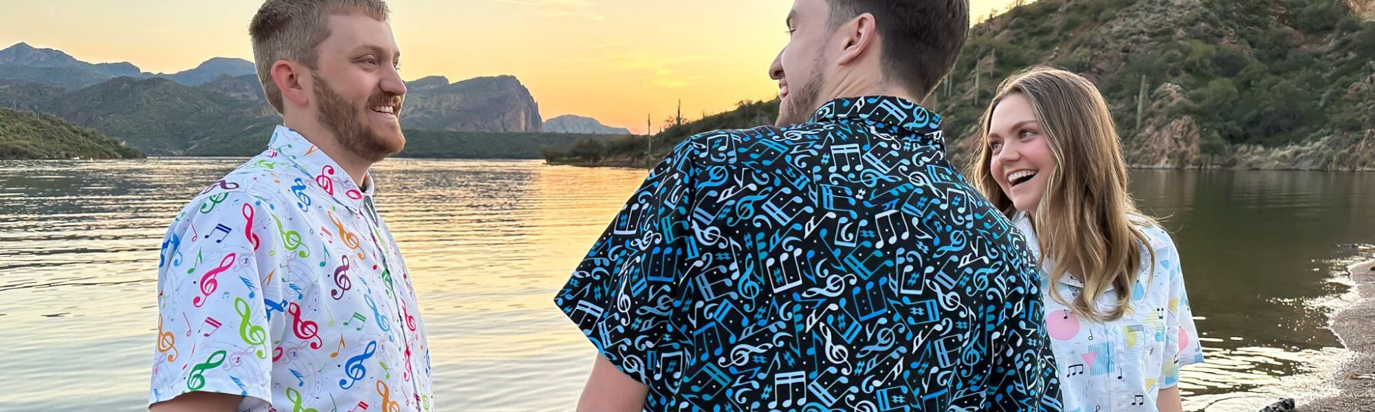 Three friends wearing their favorite geeky music themed button up shirts stand together at the edge of a lake at sunset. These shirts are perfect for music festivals or casual hangouts with fellow music enthusiasts.