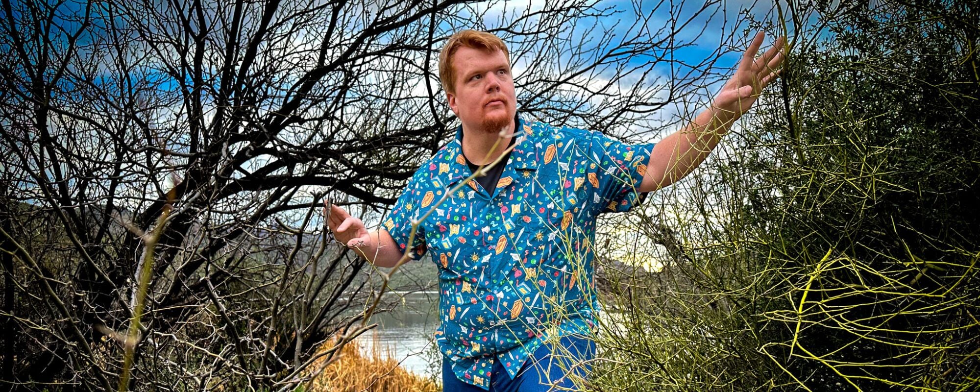 A man wearing a blue Dnd themed button-up shirt with a variety of common RPG game items including shields, weapons, maps, and potions. The shirt features a cool and unique pattern perfect for any geeky gaming enthusiast. 